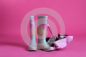 Closed umbrella and rubber boots on pink background