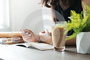 Closed up Asian woman in black dress holding pencil and thinking on blank notebook with eyeglasses, Iced coffee and old books on