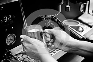 Closed up of baristaâ€™s hand holding pitcher full of milk frothing from coffee machine. For making cappuccino or latte. Black and