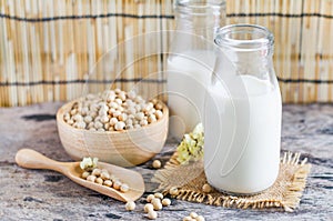 Closed up delicious homemade soybean milk in glass bottle over blur seeds in wooden bowl and spoon