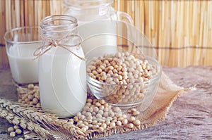 Closed up delicious homemade soybean milk in glass bottle with some seeds in glass bowl with dry wheat ear