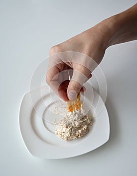 Closed up hand dipping Tuna spread in white plate with mini cracker.