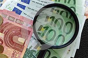 Closed up of magnifying glass on pile of Euro banknotes with Eur