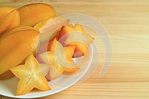 Closed up of orange yellow ripe whole fruits and sliced Star Fruit on white plate served on wooden table, with free space for text