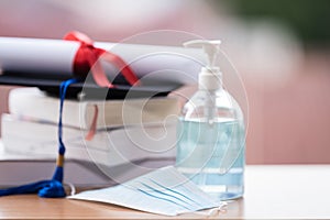 Closed-up photo of a college graduation cap mortarboard with degree diploma certificate and face mask on the table. Graduation in