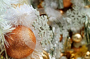Closed up pink-gold gritter ball shaped Christmas ornament with blurred silver glitter snowflake and another ornaments