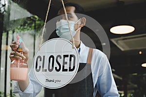 Closed. vintage sign board hanging on glass door with waitress staff wearing protective face mask cleaning and washing mirror wind