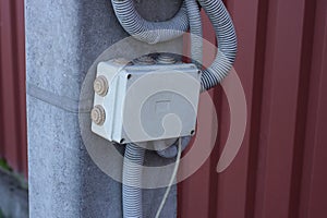 Closed white metal box and plastic hose on a gray concrete pillar against a brown wall