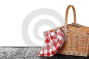 Closed wicker picnic basket with checkered tablecloth on wooden table