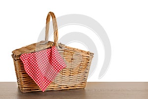 Closed wicker picnic basket with checkered tablecloth on wooden table against white