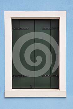 Closed window with green shutter on blue wall