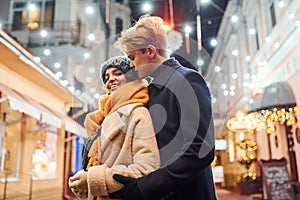 Closeness of the people. Happy young couple in warm clothes is on christmas decorated street together