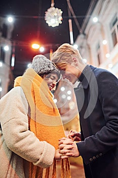 Closeness of the people. Happy young couple in warm clothes is on christmas decorated street together