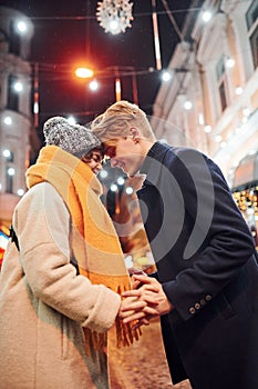 Closeness of the people. Happy young couple in warm clothes is on christmas decorated street together