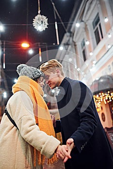 Closeness of the people. Happy young couple in warm clothes is on christmas decorated street together