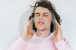 Closep portrait of attractive stylish young male with curly hair wearing pink clothes, enjoying and listening favorite music on