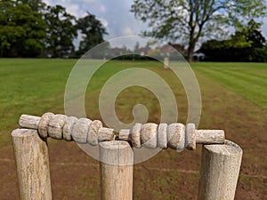 A closer up of cricket stumps and bails on a muddy strip