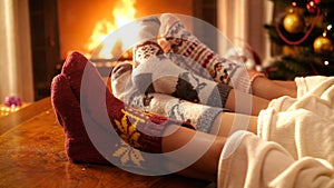 Closeup 4k footage of people in wool socks holding feet next to burning fire in fireplace at night. People relaxing on