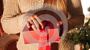 Closeup 4k footage of toung woman opening red box with gift and looking inside. Perfect shot for Christmas or New Year