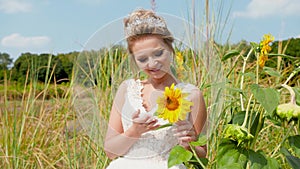 Closeup 4k video of beautiful smiling bride holding yellow sunflower and posing in field at brights sunny summer day