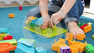 Closeup 4k video of little toddler boy playing with colorful building bricks and blocks on floor at home