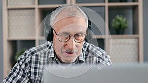 Closeup 70s grandfather in headphones talking online video call with doctor use laptop pc