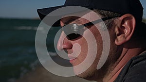closeup of adult male in cap in meditation state of mind with reflection on sea waves in sunglasses during outdoor