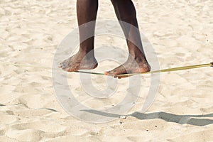 Closeup African American man feet walking on tightrope or slackline on sandy background. Slacklining is a practice in photo