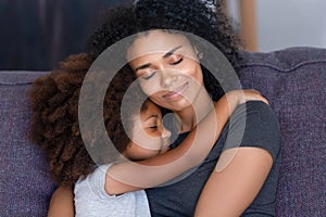 Closeup african daughter embracing mother sitting on couch at home