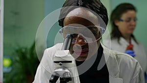 Closeup of african researcher woman looking at leaf slide under microscope