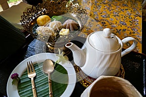 Closeup afternoon tea time set of Thai traditional dessert with banana leaf and flower decoration on floral pattern table cloth