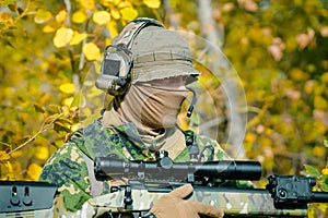 Closeup airsoft man in uniform hold sniper rifle on yellow forest backdrop. Side view photo