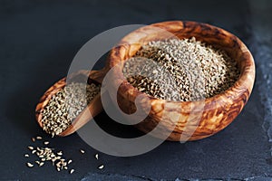 Closeup of ajwain seeds in a wooden bowl over darl slate background