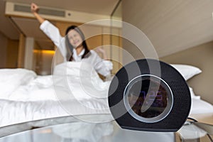 Closeup alarm clock having a good day with happy woman stretching in bed after waking up in morning. selective focus