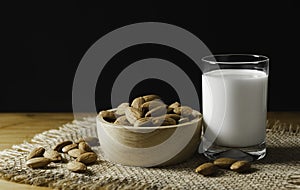 Closeup almonds in wooden bowl and glass milk on wooden background with copy space