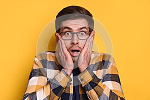 Closeup of amazed handsome guy in glasses isolated over yellow background