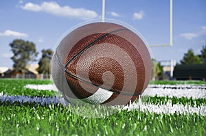 Closeup of American football on field with goal post