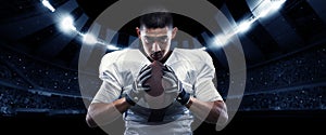Closeup american football player in sports equipment grips the ball tightly against night stadium with spotlights