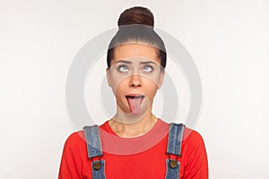 Closeup of amusing funny girl with hair bun looking up with eyes crossed and demonstrating tongue out