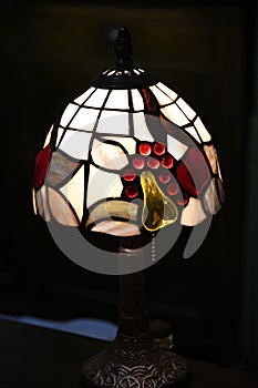 Closeup of antique table lamp with stained glass lampshade on black background. Glowing mosaic lamp in shape of dome. Vintage