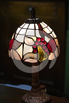 Closeup of antique table lamp with stained glass lampshade on black background. Glowing mosaic lamp in shape of dome. Vintage