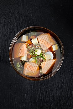 Closeup on appetizing ishikari miso soup with salmon in a black bowl, on black background, japanese food.