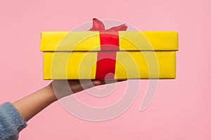 Closeup of arm in warm sweater holding wrapped yellow gift box with red stripe, delivery of present on holidays photo