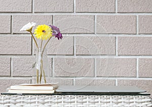 Closeup artificial colorful flower on transparent glass bottle on wood weave table on blurred brown brick wall texture background