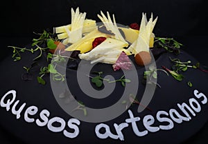 Closeup of Artisan cheese on a black plate with herbs and Spanish text Quesos artesanos photo