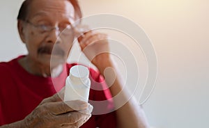 Closeup of Asian elderly male with presbyopia holding and looking at a pill container with confusion