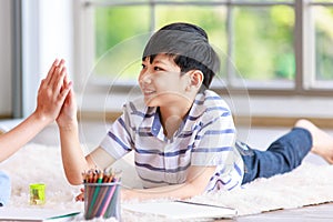 Closeup Asian happy cheerful joyful little boy sitting laying lying down on carpet floor high five together while painting drawing