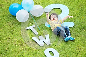 Closeup happy asian kid lie on grass floor in park textured background in 2 nd years anniversary concept