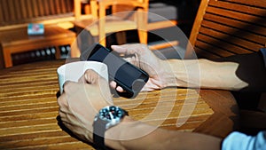 Closeup of Asian male hands playing smartphone and drinking coffee at an outdoor table with morning sunlight.selected focus