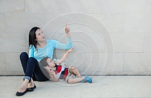 Closeup asian mother pointing her finger and tell her son to look at space on marble stone wall textured background
